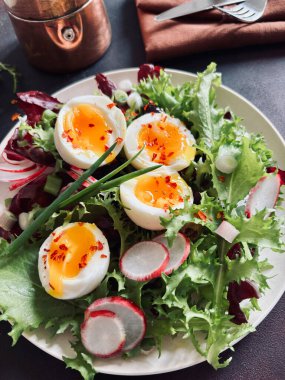Beyaz tabakta servis edilen haşlanmış yumurtalarla birlikte taze sağlıklı sebze salatası, koyu arkaplan. Tam üstte.