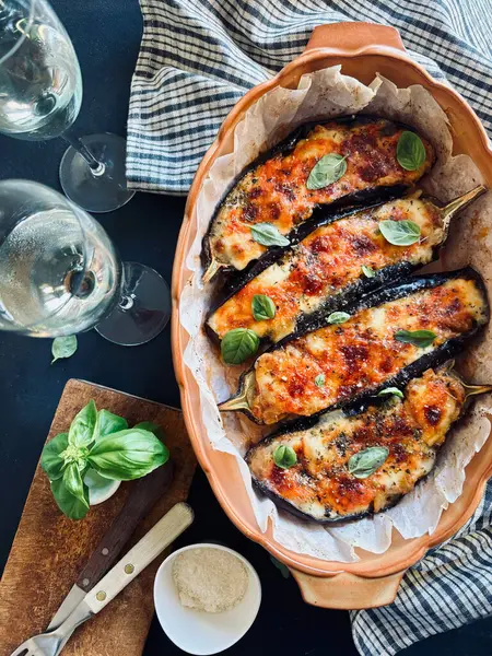 Mozarella peynirli ev yapımı fırında patlıcan, doğranmış domates ve koyu arkaplanda taze fesleğen yaprakları. Vejetaryen yemeği. Tam üstte.