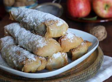 Elma köfteleri, fındık ve elmaların yanına beyaz bir tabağa krema serpiştirilmiş şeker serpiştirilmiş. Mini strudel veya Yunan Milopitakia ruloları.