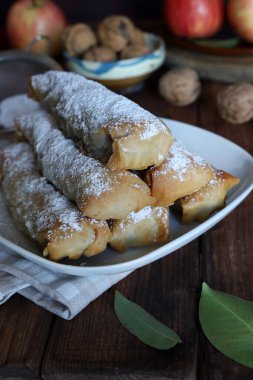 Elma köfteleri, fındık ve elmaların yanına beyaz bir tabağa krema serpiştirilmiş şeker serpiştirilmiş. Mini strudel veya Yunan Milopitakia ruloları.