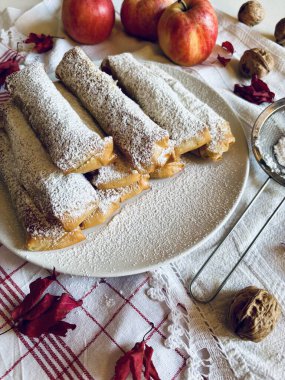 Elma köfteleri, fındık ve elmaların yanına beyaz bir tabağa krema serpiştirilmiş şeker serpiştirilmiş. Mini strudel veya Yunan Milopitakia ruloları.
