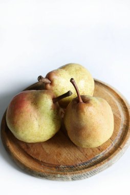 Tahta bir kesme tahtasının üzerinde üç olgun armut, beyaz arkaplan. Sağlıklı ve vejetaryen yemekleri. Boşluğu kopyala.