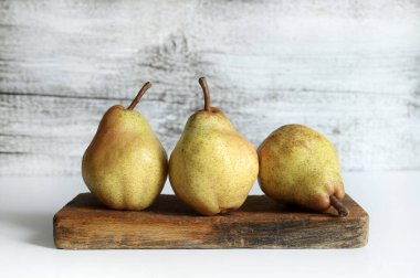 Tahta kesme tahtasının üzerinde üç olgun armut, beyaz ahşap zemin. Sağlıklı ve vejetaryen yemekleri. Boşluğu kopyala.