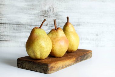 Tahta kesme tahtasının üzerinde üç olgun armut, beyaz ahşap zemin. Sağlıklı ve vejetaryen yemekleri. Boşluğu kopyala.