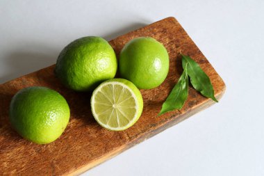 Ahşap kesim tahtasının üzerinde yaprakları olan bir grup taze kireç meyvesi gri ışıklı arka planda izole edilmiş. Sağlıklı gıda konsepti. Boşluğu kopyala.