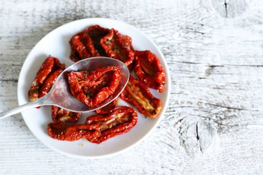 Ahşap arka planda izole edilmiş bir grup kurutulmuş domates. Ön plana odaklan. Zeytinyağı ve bitkilerle kurutulmuş domates dilimleri. İtalyan yemeği. Tam üstte. Boşluğu kopyala.