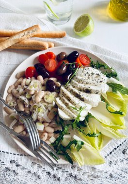 Geleneksel Akdeniz ton balığı salatası taze domates, zeytin, mozzarella, masada beyaz bir kasede fasulye. Sağlıklı gıda konsepti.