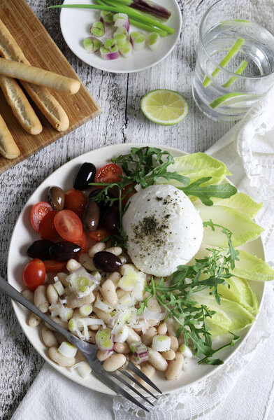 Традиционный средиземноморский салат из тунца со свежими помидорами, оливками, моцареллой, фасолью в белой миске на столе. Концепция здорового питания.