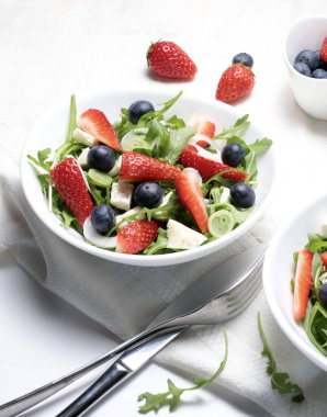 Beyaz tabakta roka, böğürtlen ve beyaz peynirli çilek salatası. Yaz yemeği. Sağlıklı ve vejetaryen yemekleri. Tam üstte.