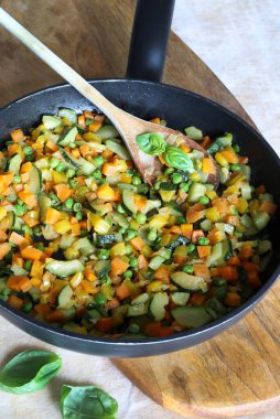 Tahta kesme tahtasının üzerinde karışık sebzeli kızartma tavası. Havuç, biber, kabak ve otlar. Sağlıklı bir meze. Tam üstte.