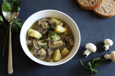 Siyah arka planda beyaz kasede mantar, patates ve otlu lezzetli çorba. Sağlıklı ve vejetaryen yemekleri. Tam üstte
