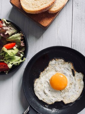 A single fried egg in a frying pan served with vegetables and bread on a gray background. Healthy food concept. Directly above