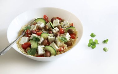 Beyaz arka planda beyaz bir kasede servis edilen domates, salatalık ve biber gibi taze sebzeli kuskus. Sağlıklı ve vejetaryen yemekleri.