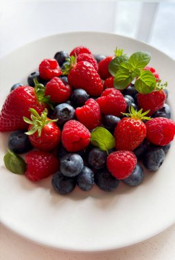 Taze meyveler. Beyaz arka planda izole edilmiş bir tabakta çilek, yaban mersini ve ahududu. Sağlıklı yiyecekler. Tam üstte.
