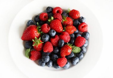 Taze meyveler. Beyaz arka planda izole edilmiş bir tabakta çilek, yaban mersini ve ahududu. Sağlıklı yiyecekler. Tam üstte.