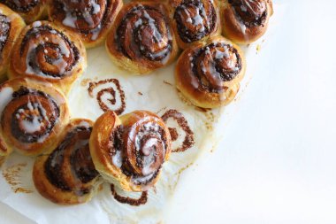 Beyaz ahşap bir masanın üzerindeki krema peçesiyle süslenmiş cevizli çörek rulosu. Tarçınlı rulo. Nuss-schnecke (Ceviz salyangozları).