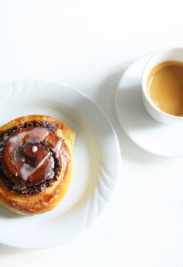 Tarçınlı rulo. Beyaz ahşap arka planda krema ve bir fincan kahveyle süslenmiş cevizli çörek rulosu. Nuss-schnecke Ceviz salyangozları.