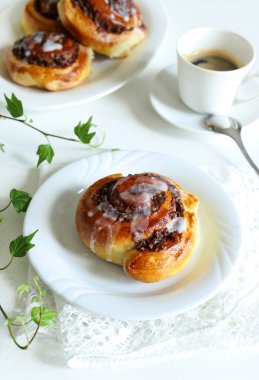 Tarçınlı rulo. Beyaz ahşap arka planda krema ve bir fincan kahveyle süslenmiş cevizli çörek rulosu. Nuss-schnecke Ceviz salyangozları.
