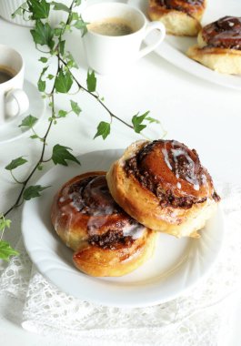 Tarçınlı rulo. Beyaz ahşap arka planda krema ve bir fincan kahveyle süslenmiş cevizli çörek rulosu. Nuss-schnecke Ceviz salyangozları.