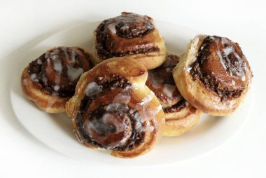 Beyaz ahşap bir masanın üzerindeki krema peçesiyle süslenmiş cevizli çörek rulosu. Tarçınlı rulo. Nuss-schnecke (Ceviz salyangozları).