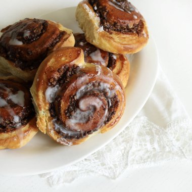 Beyaz ahşap bir masanın üzerindeki krema peçesiyle süslenmiş cevizli çörek rulosu. Tarçınlı rulo. Nuss-schnecke (Ceviz salyangozları).