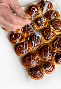 Beyaz ahşap bir masanın üzerindeki krema peçesiyle süslenmiş cevizli çörek rulosu. Tarçınlı rulo. Nuss-schnecke (Ceviz salyangozları).