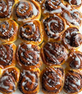 Beyaz ahşap bir masanın üzerindeki krema peçesiyle süslenmiş cevizli çörek rulosu. Tarçınlı rulo. Nuss-schnecke (Ceviz salyangozları).