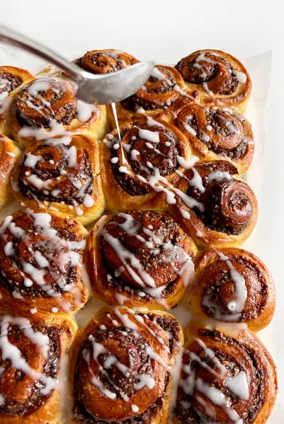 Beyaz ahşap bir masanın üzerindeki krema peçesiyle süslenmiş cevizli çörek rulosu. Tarçınlı rulo. Nuss-schnecke (Ceviz salyangozları).