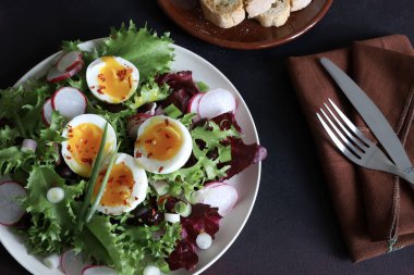 Beyaz tabakta servis edilen haşlanmış yumurtalarla birlikte taze sağlıklı sebze salatası, koyu arkaplan. Tam üstte.