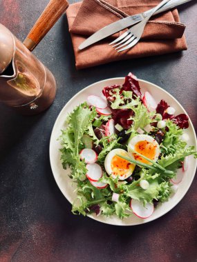 Beyaz tabakta servis edilen haşlanmış yumurtalarla birlikte taze sağlıklı sebze salatası, koyu arkaplan. Tam üstte.