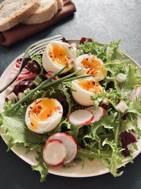 Beyaz tabakta servis edilen haşlanmış yumurtalarla birlikte taze sağlıklı sebze salatası, koyu arkaplan. Tam üstte.