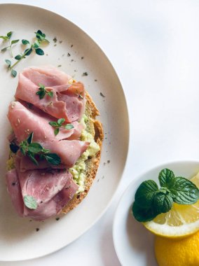 Prosciutto, otlar ve limonlu beyaz arka planda lezzetli avokado tostu. Sağlıklı yiyecekler. Tam üstte.