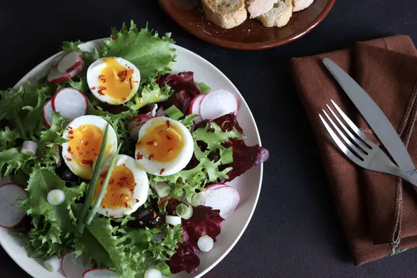 Beyaz tabakta servis edilen haşlanmış yumurtalarla birlikte taze sağlıklı sebze salatası, koyu arkaplan. Tam üstte.