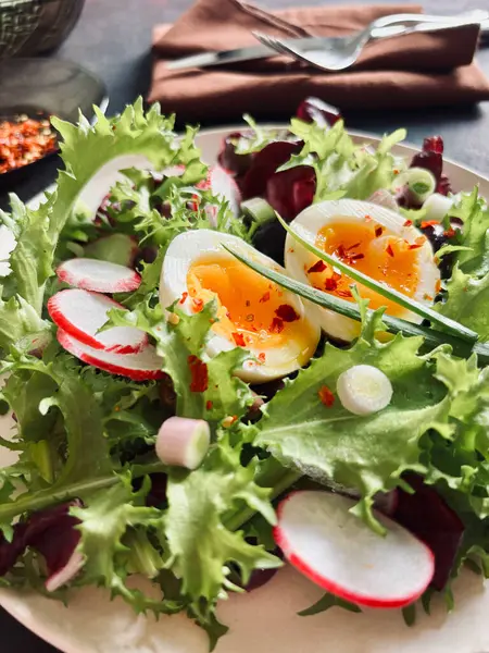 Beyaz tabakta servis edilen haşlanmış yumurtalarla birlikte taze sağlıklı sebze salatası, koyu arkaplan. Tam üstte.