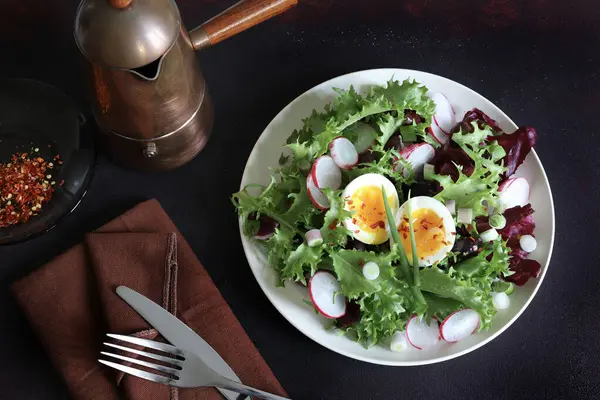 Beyaz tabakta servis edilen haşlanmış yumurtalarla birlikte taze sağlıklı sebze salatası, koyu arkaplan. Tam üstte.