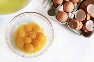 Ayrı yumurta sarıları ve cam kaselerde beyaz yumurta sarıları ve arka planda kırık yumurta kabukları ve bütün yumurtalar. Tam üstte.