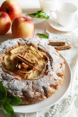 Masanın arkasında tarçın çubukları ve taze elmalarla süslenmiş yumuşak ve lezzetli ev yapımı elmalı turta. Tam üstte.