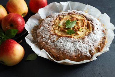 Yumuşak ve lezzetli ev yapımı elmalı turta, gri arka planda taze elmalar. Tam üstte.