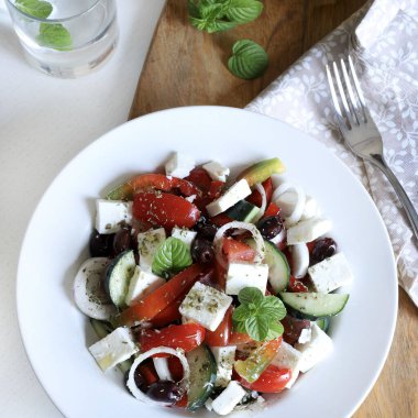 Beyaz peynirli Yunan salatası ve domates, biber, salatalık, soğan, zeytin ve ahşap masadaki kekik gibi taze sebzeler. Sağlıklı ve vejetaryen yemekleri.