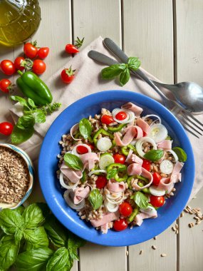 Jambonlu ve taze sebzeli yaz salatası. Domates, soğan, biber ve ahşap masadaki taze fesleğen gibi. Sağlıklı yiyecekler. Tam üstte.