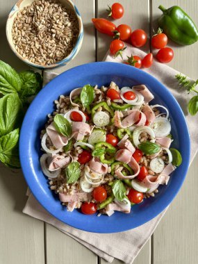 Jambonlu ve taze sebzeli yaz salatası. Domates, soğan, biber ve ahşap masadaki taze fesleğen gibi. Sağlıklı yiyecekler. Tam üstte.