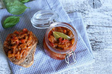 Zacusca - geleneksel Romen yayılımı. Kremalı sebze soslu cam bir kavanoz, patlıcan, soğan, domates ve ahşap zemin üzerinde kavrulmuş biber..