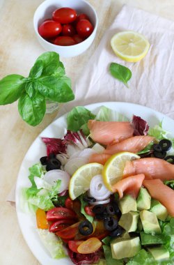 Somon füme salata, avokado, zeytin, limon, marul ve beyaz tabakta taze sebze. Sağlıklı yiyecekler. Tam üstte.