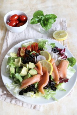 Somon füme salata, avokado, zeytin, limon, marul ve beyaz tabakta taze sebze. Sağlıklı yiyecekler. Tam üstte.