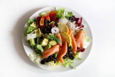 Somon füme salata, avokado, zeytin, limon, marul ve beyaz tabakta taze sebze. Sağlıklı yiyecekler. Tam üstte.