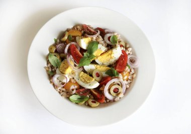 Homemade spelled salad with boiled eggs, fresh vegetables and basil on a white background. Spelt salad. Healthy food. Directly above.