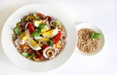 Homemade spelled salad with boiled eggs, fresh vegetables and basil on a white background. Spelt salad. Healthy food. Directly above.
