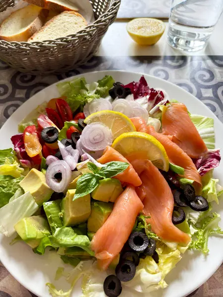 Somon füme salata, avokado, zeytin, limon, marul ve beyaz tabakta taze sebze. Sağlıklı yiyecekler. Tam üstte.