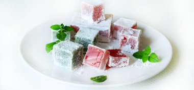 Türk lokumu. Lokum, renkli, aromalı, pudra şekeriyle kaplanmış jöle aromalı şekerler beyaz bir masada servis edilir. Nane yaprakları dekorasyon.