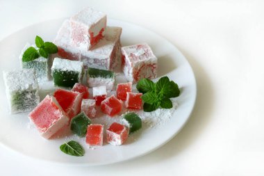 Türk lokumu. Lokum, renkli, aromalı, pudra şekeriyle kaplanmış jöle aromalı şekerler beyaz bir masada servis edilir. Nane yaprakları dekorasyon.